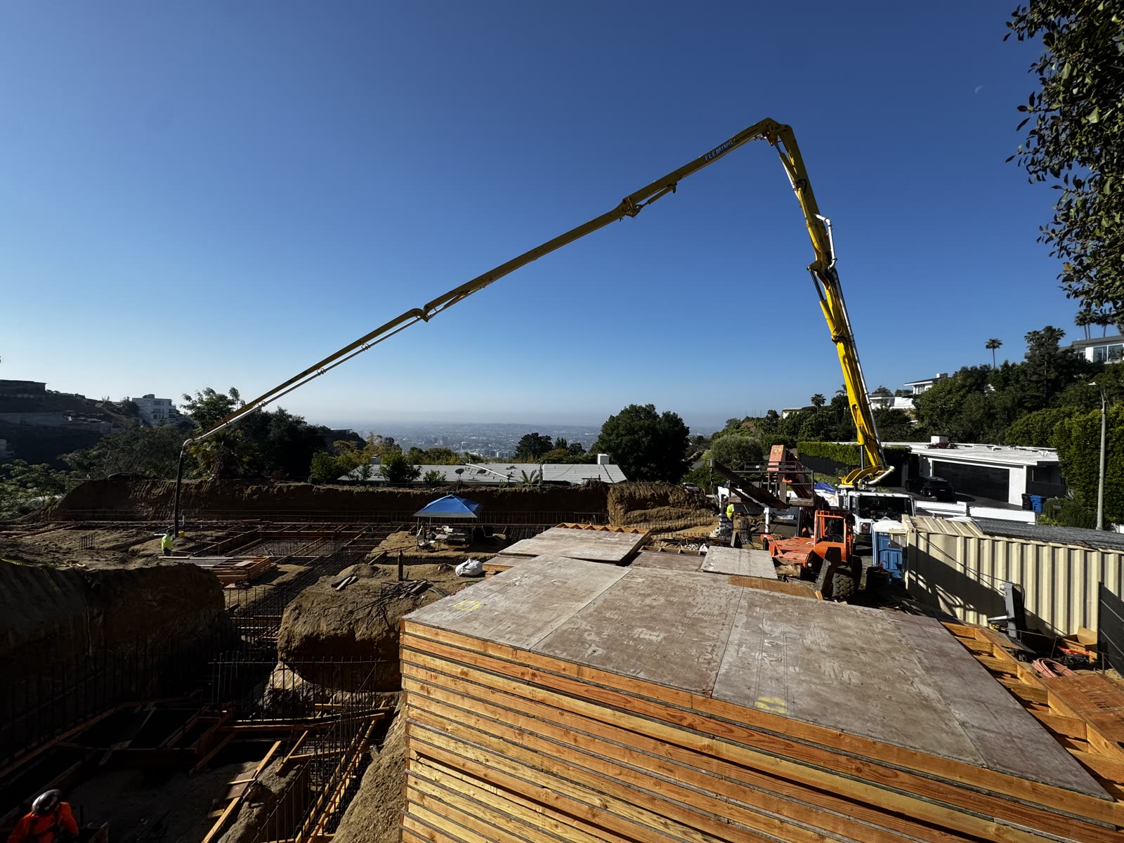 Concrete pump boom reaching over formed hillside foundation walls on a Los Angeles jobsite