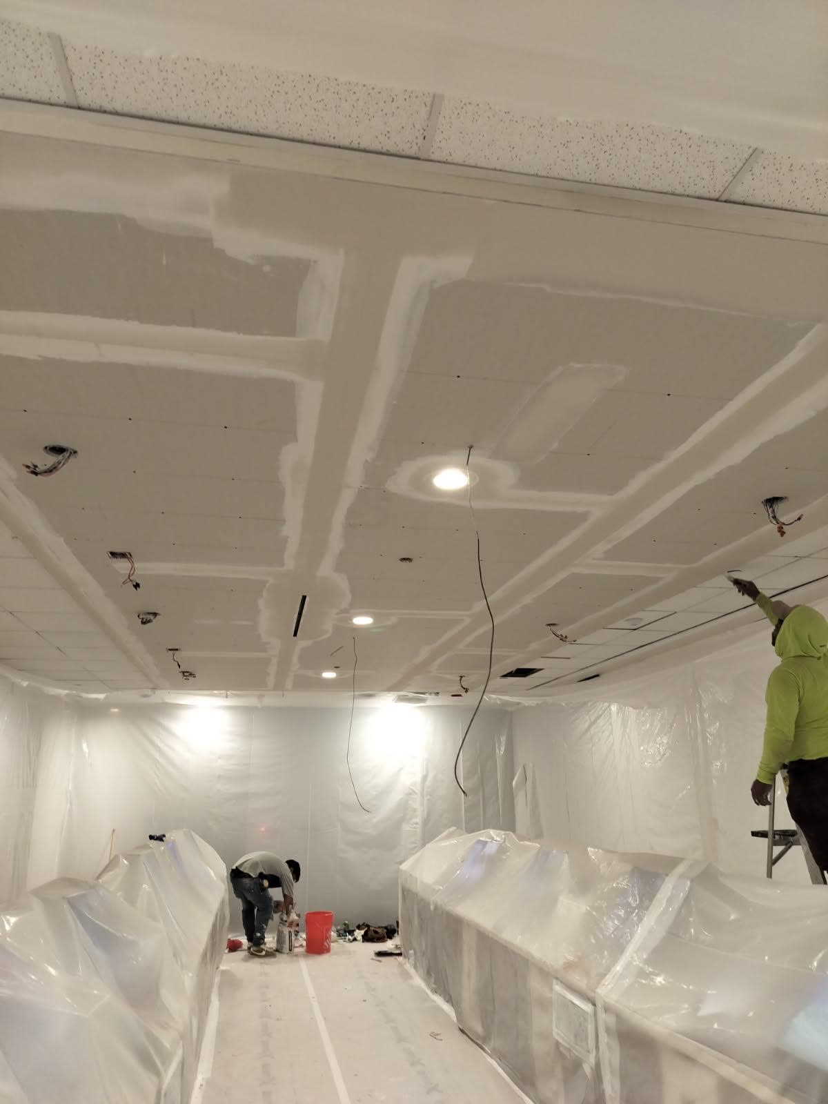 Crew taping and finishing a new drywall ceiling inside a fully masked work area