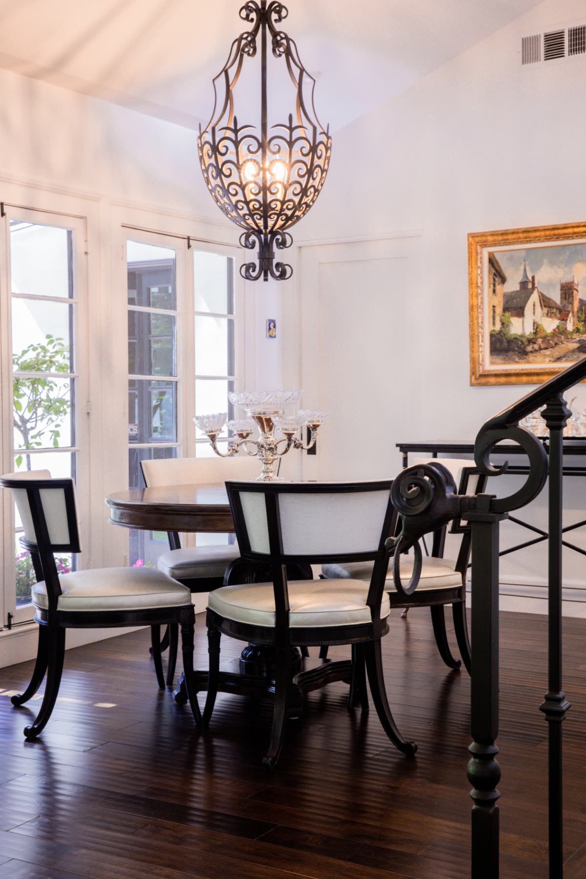 Elegant dining room with white walls, dark wood flooring, and ornate chandelier