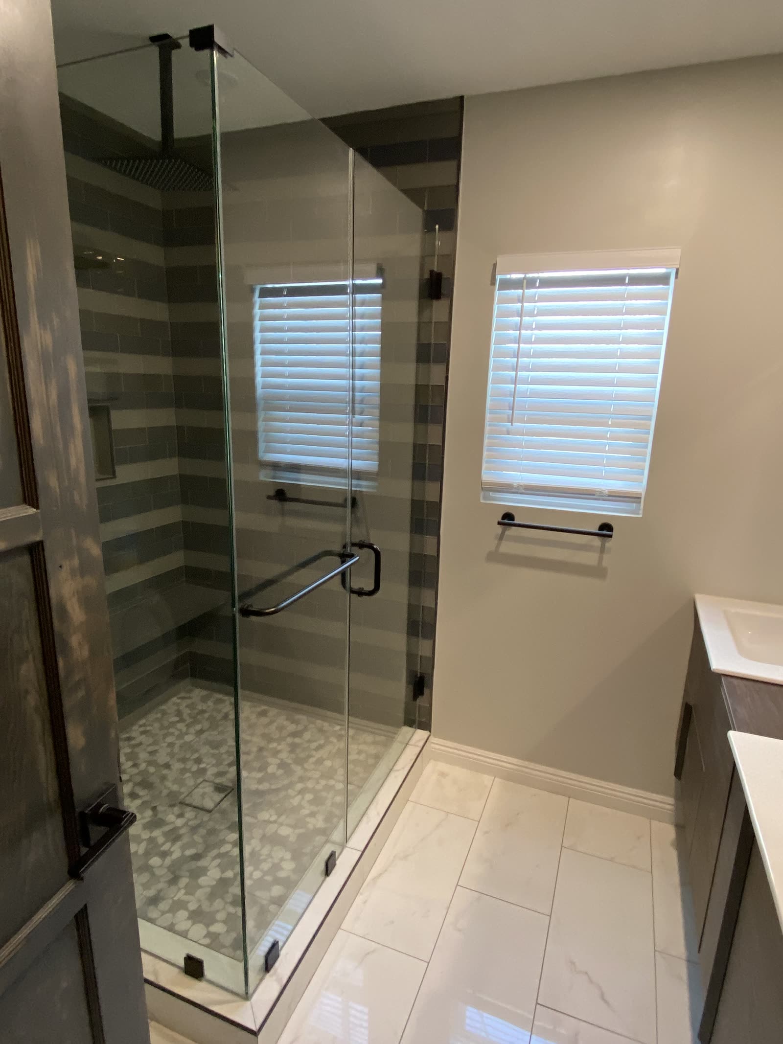 Remodeled shower with frameless glass enclosure, banded tile walls, and pebble floor