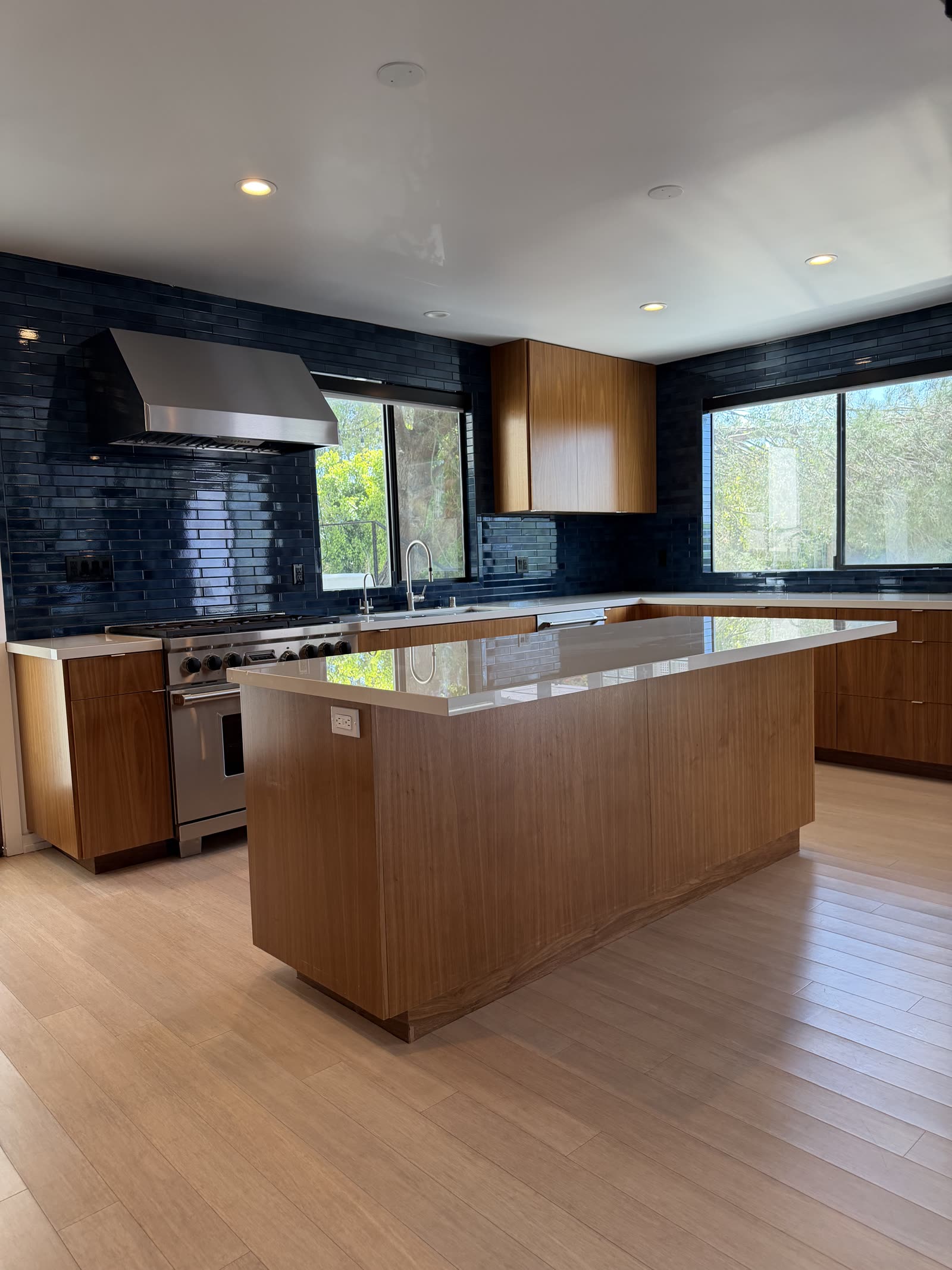Modern kitchen with walnut cabinetry, waterfall island, and glossy navy tile backsplash